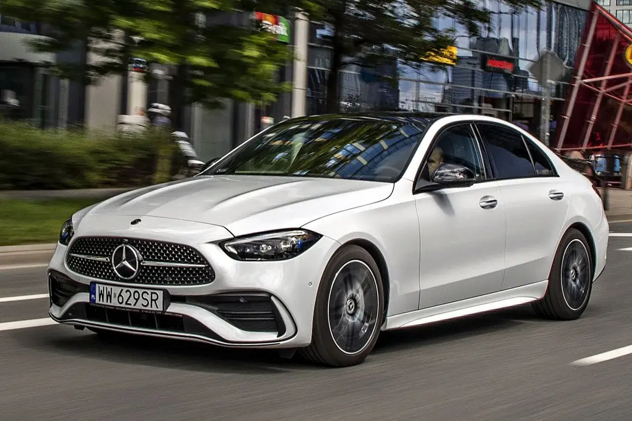 Biały Mercedes-Benz Klasy C porusza się po mieście, odbijając światła budynków w swojej lśniącej karoserii.
