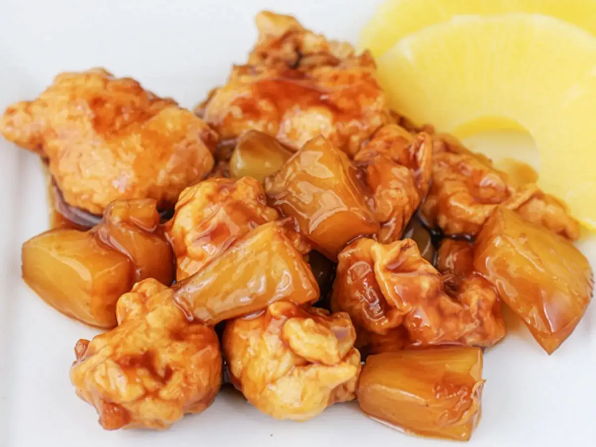 Sabroso pollo con piña en salsa agridulce, con trozos dorados y rodajas de piña fresca al lado.
