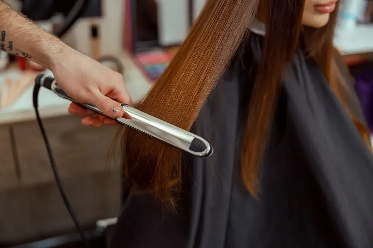 Stylista tworzy fale na długich, brązowych włosach, używając prostownicy. Pokazano, jak zrobić loki prostownicą.
