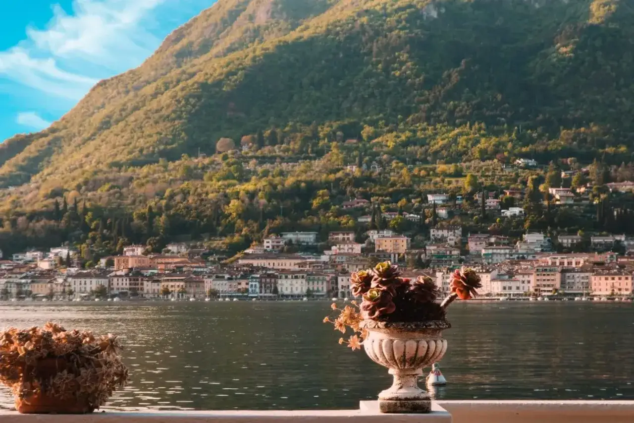 Vista di Salò sul Lago di Garda, con case colorate che si arrampicano sulla collina verdeggiante. Vasi di fiori adornano il primo piano.