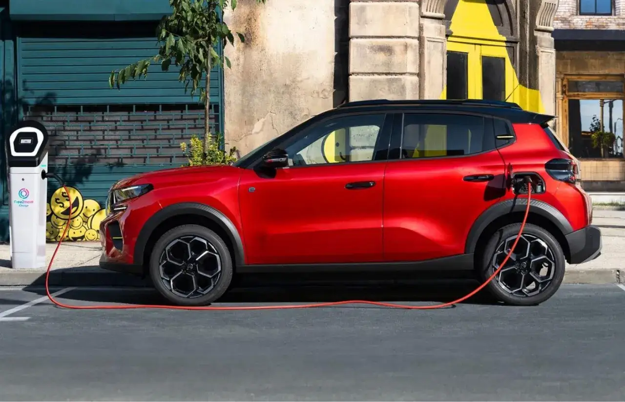 Essai R5 électrique : une voiture rouge vif branchée à une borne de recharge, prête pour l'aventure urbaine.