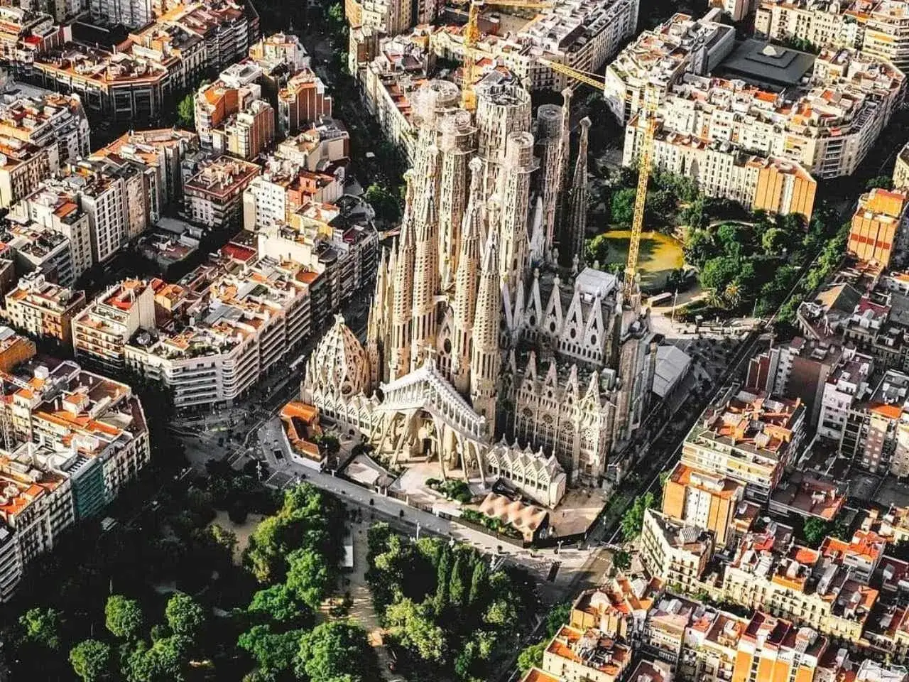 Widok z lotu ptaka na Sagrada Familia, arcydzieło Gaudiego w Barcelonie, otoczone gęstą zabudową miejską i zielenią.