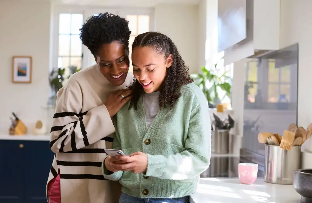 M&egrave;re et fille souriantes regardant un t&eacute;l&eacute;phone. Elles discutent peut-&ecirc;tre de la pension alimentaire jusqu'&agrave; quel &acirc;ge.