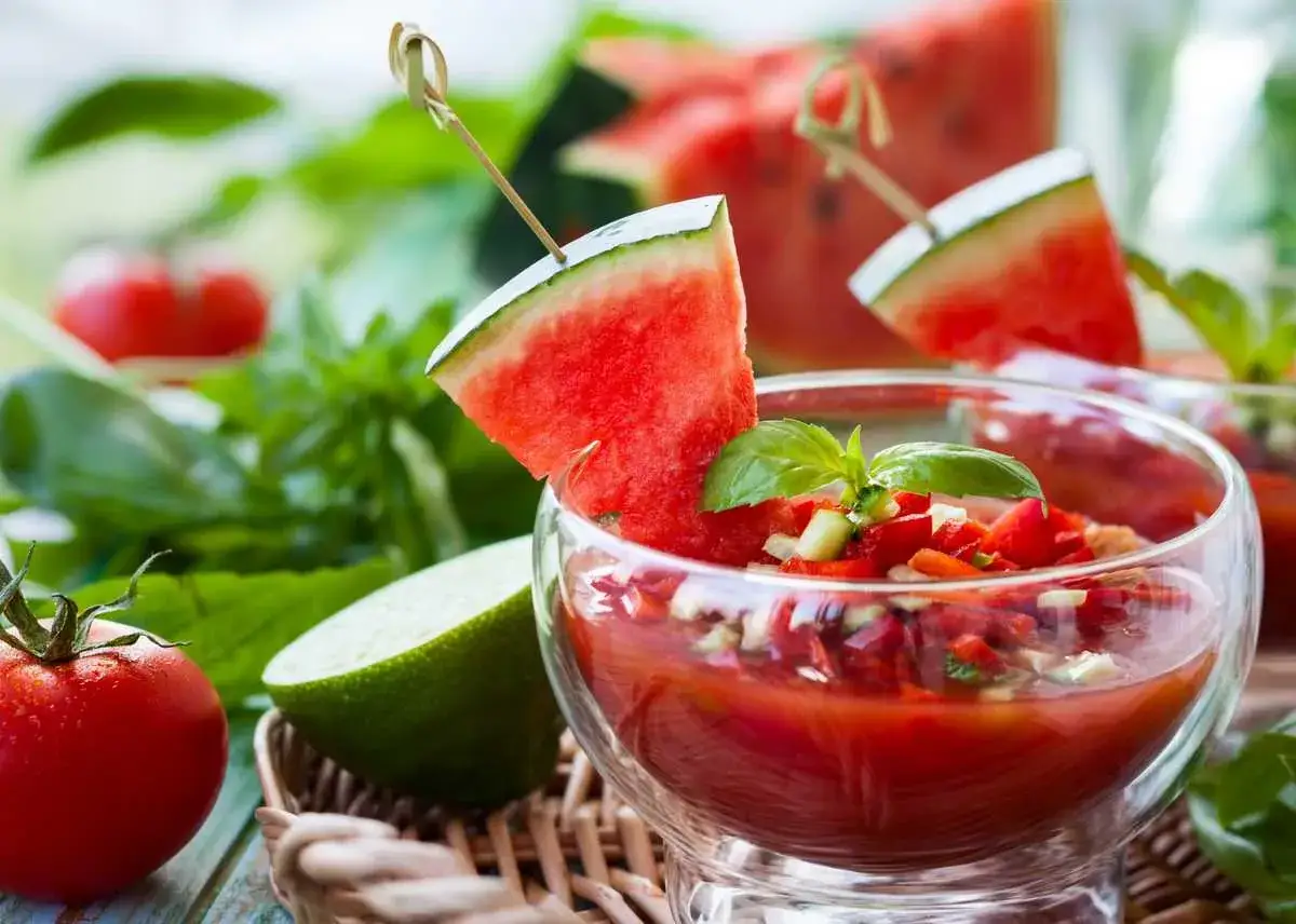 Refrescante gazpacho de sandía con trocitos de tomate, pepino y pimiento, decorado con una rodaja de sandía y hojas de albahaca.