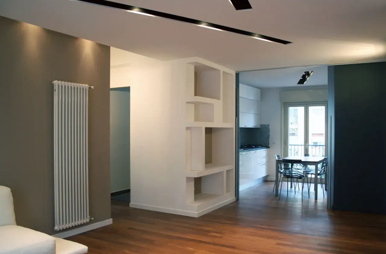Un moderno soggiorno con radiatore bianco e un'elegante libreria a nicchie. Si nota uno stacco tra parete e soffitto.