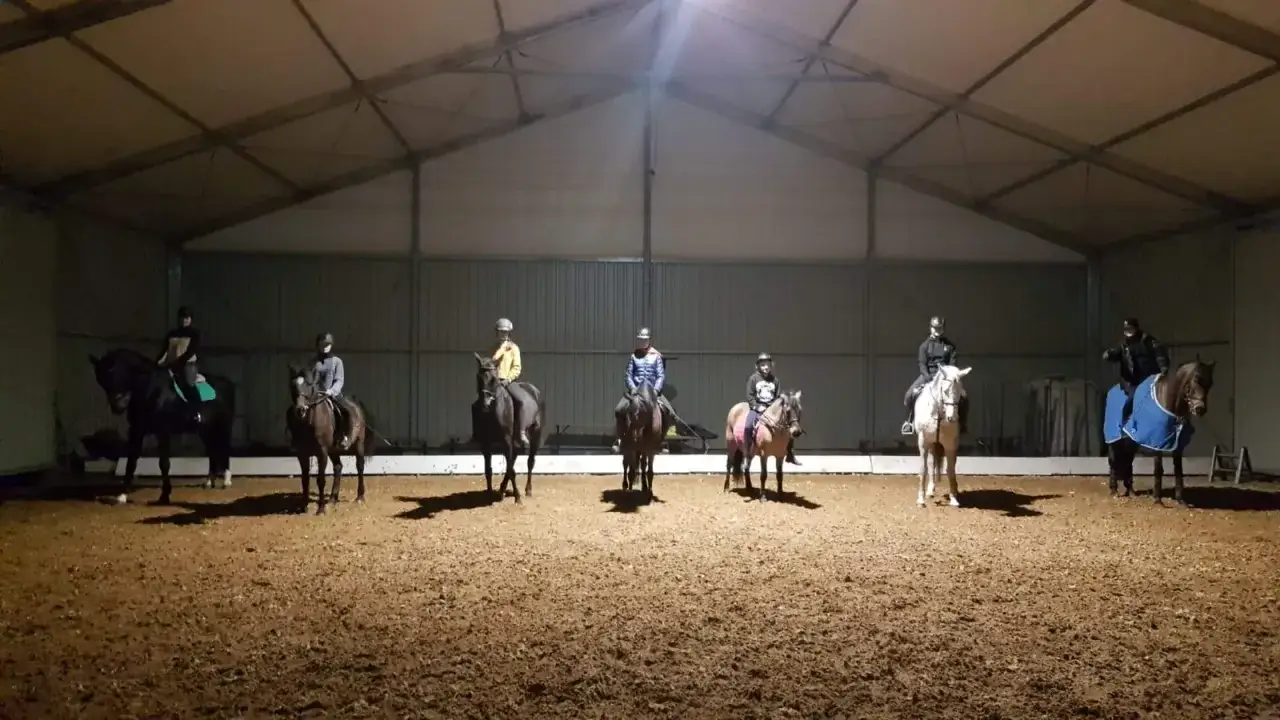 Jazda konna w hali w Osiecznej. Grupa jeźdźców na koniach podczas treningu.
