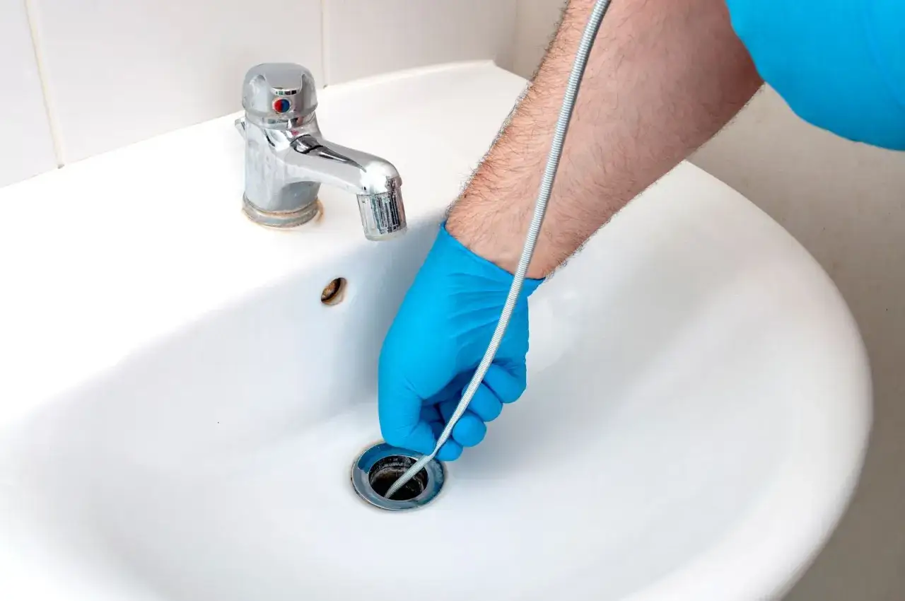 Main bleue utilisant un furet pour d&eacute;boucher un lavabo.