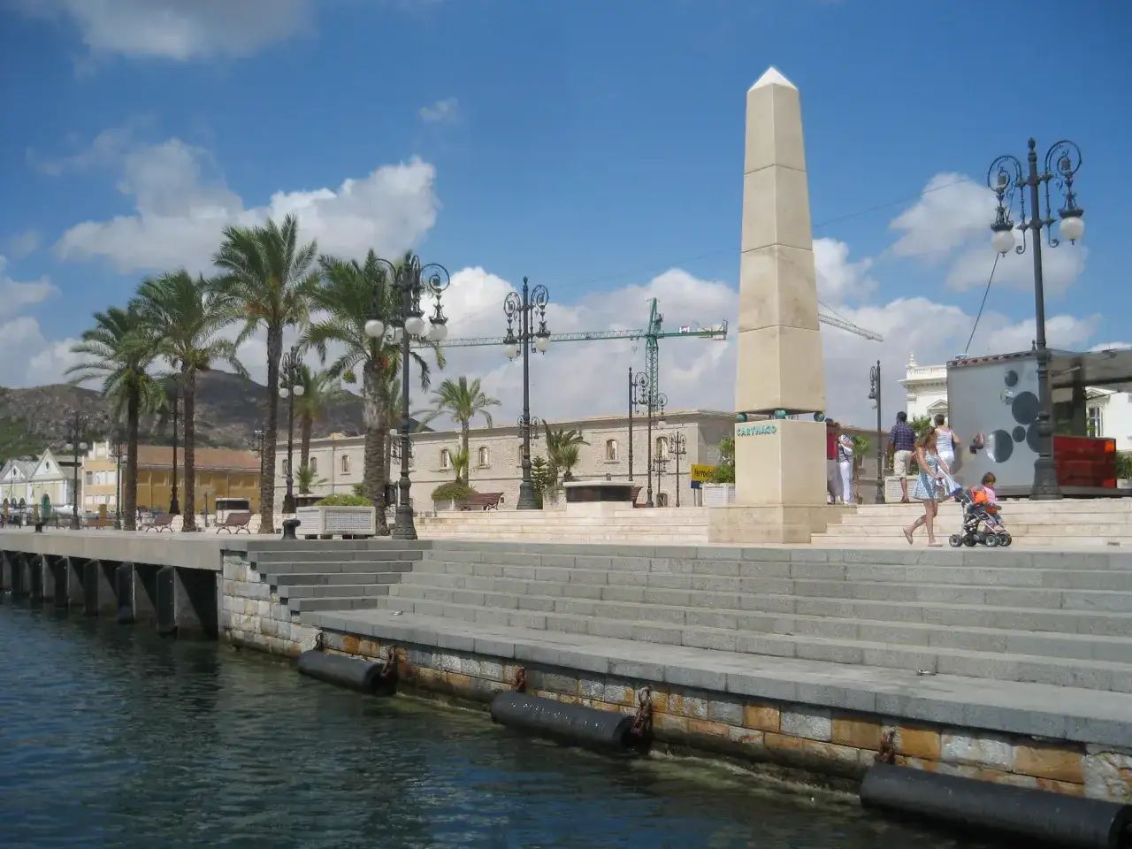 Ein sonniger Tag im Cartagena Hafen. Palmen s&auml;umen die Promenade, ein Obelisk ragt in den blauen Himmel.