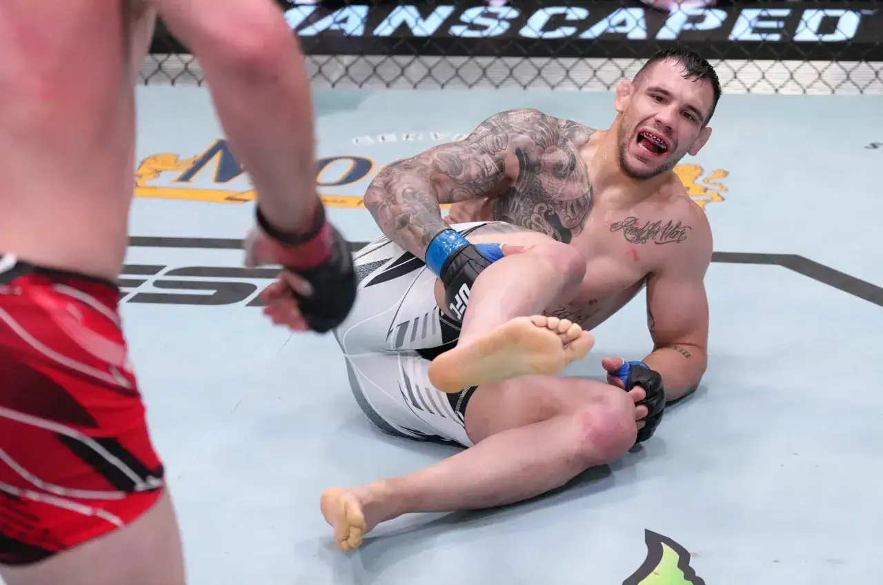 Aleksandar Rakić i hans vita UFC-shorts, med en motst&aring;ndare i r&ouml;tt i f&ouml;rgrunden. Rakić sitter p&aring; mattan, med en skadad kn&auml;.
