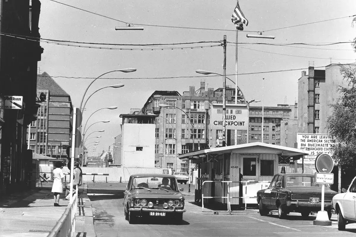 Checkpoint Charlie, Berlin. Autos passieren den Grenz&uuml;bergang. Ein Schild warnt: 