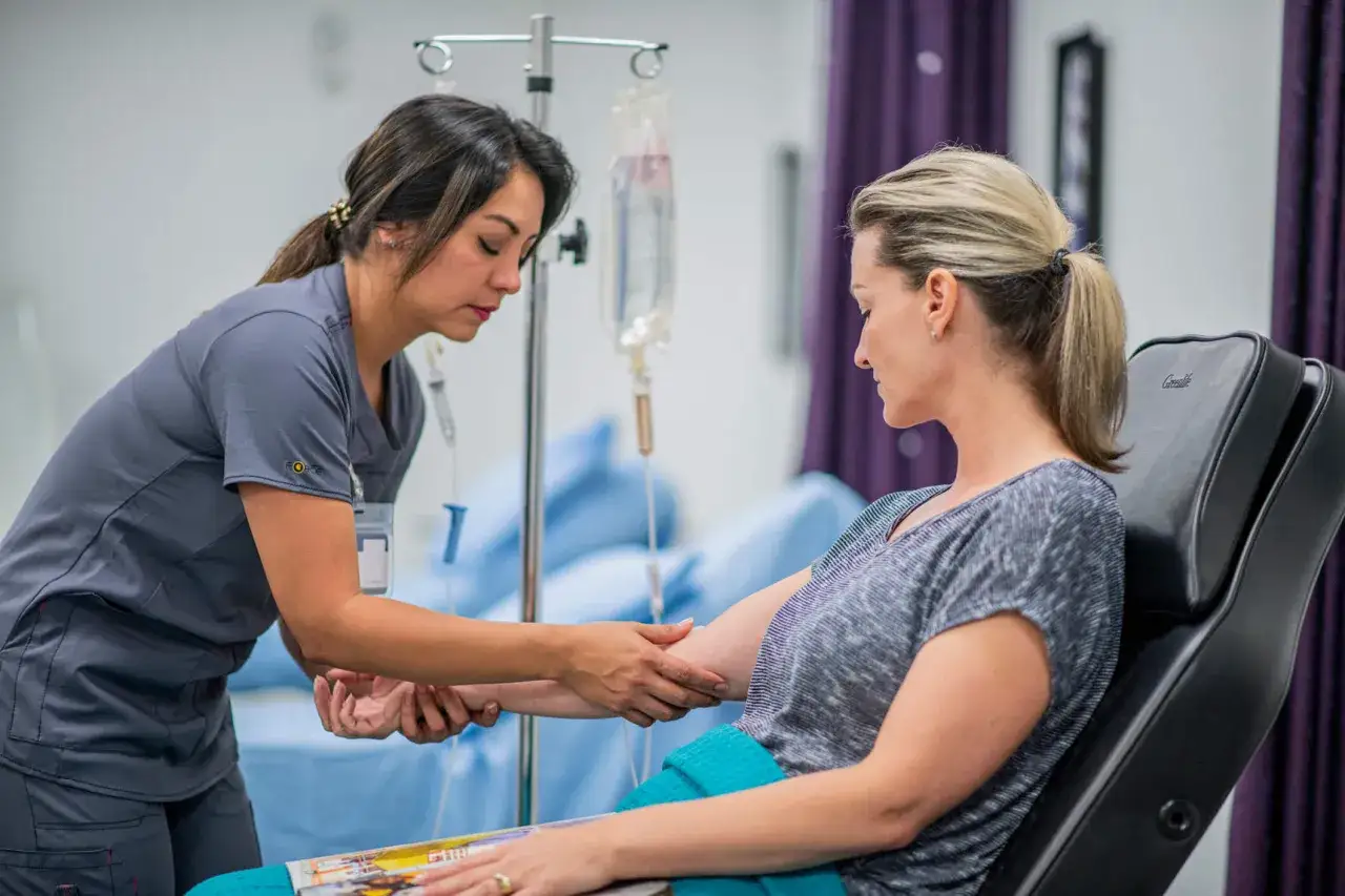 Pflegekraft bereitet Infusion mit Pembrolizumab 200 mg vor. Patientin sitzt in einem Sessel.