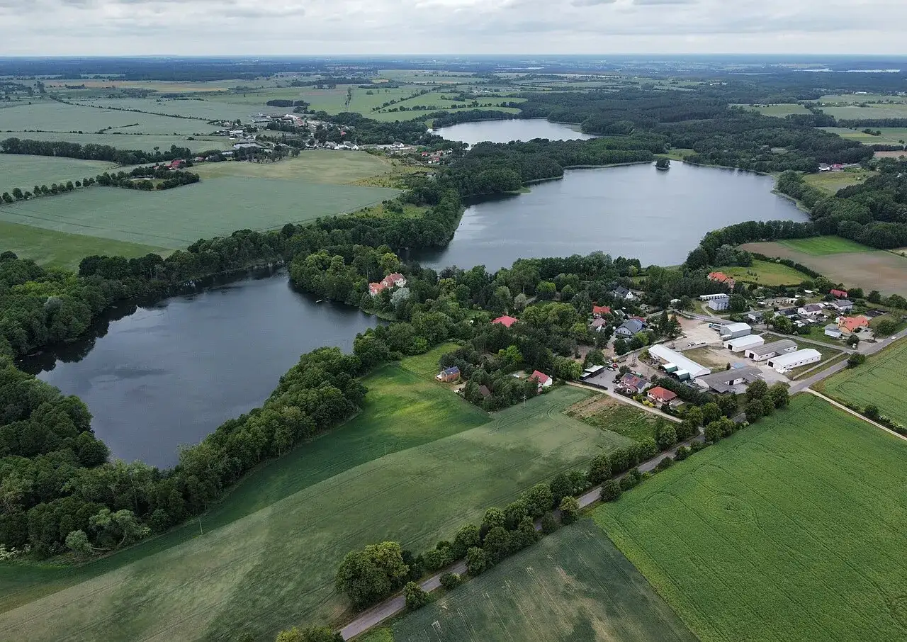 Malownicze jezioro Zajączkowskie otoczone lasami i polami, z widocznymi domami i zabudowaniami.