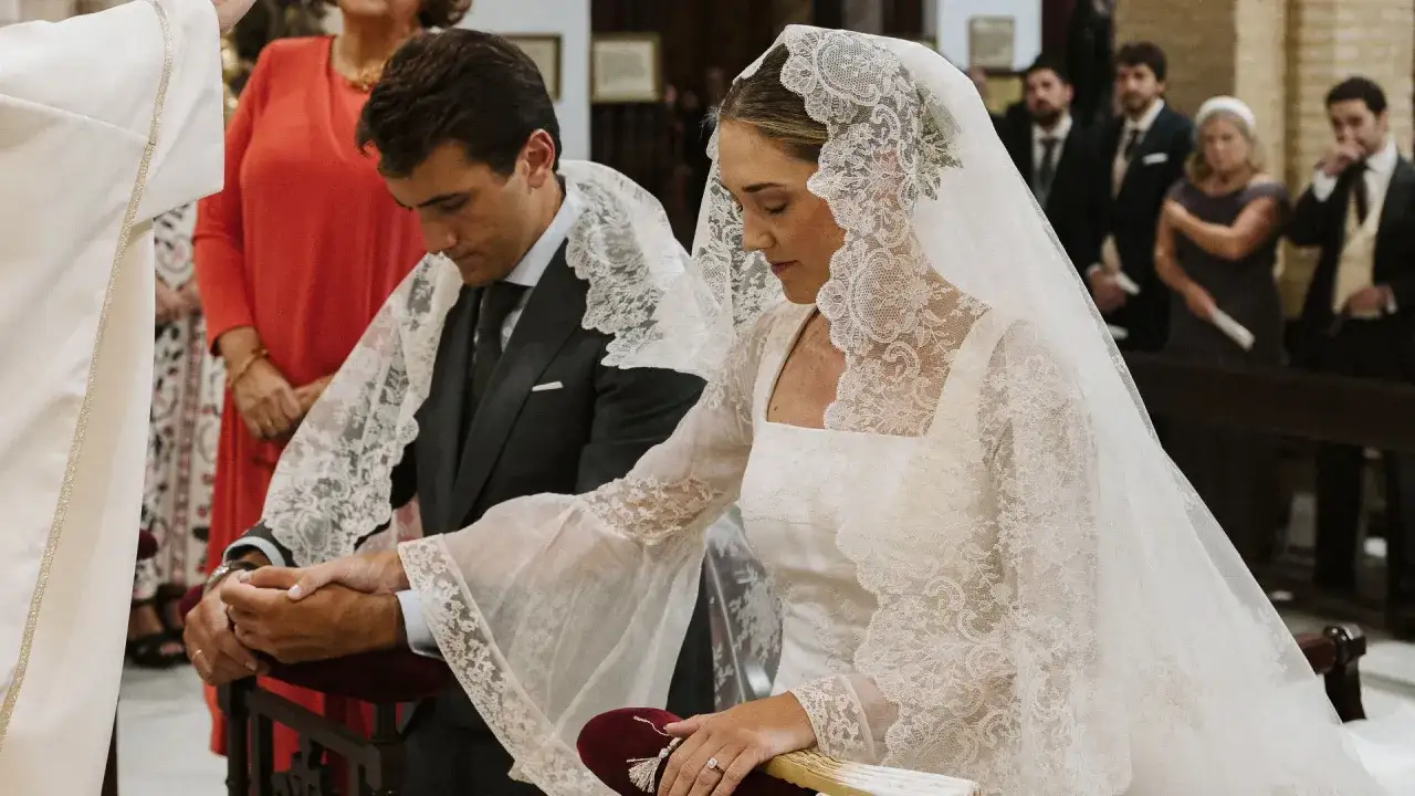 Novios tomados de la mano durante el rito de la velación, con velo de encaje y traje formal.
