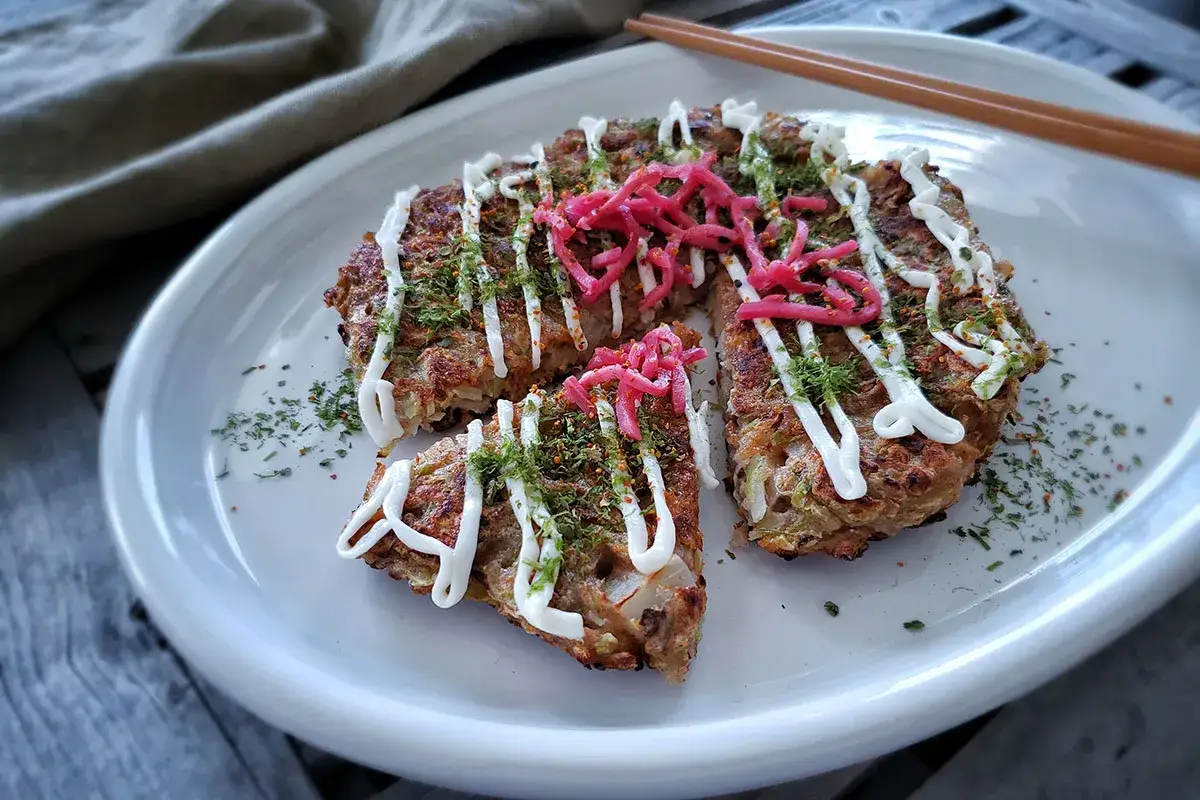 En tallrik med okonomiyaki, toppad med majonn&auml;s, picklad ingef&auml;ra och str&ouml;ssel. Perfekt f&ouml;r ett snabbt okonomiyaki recept.