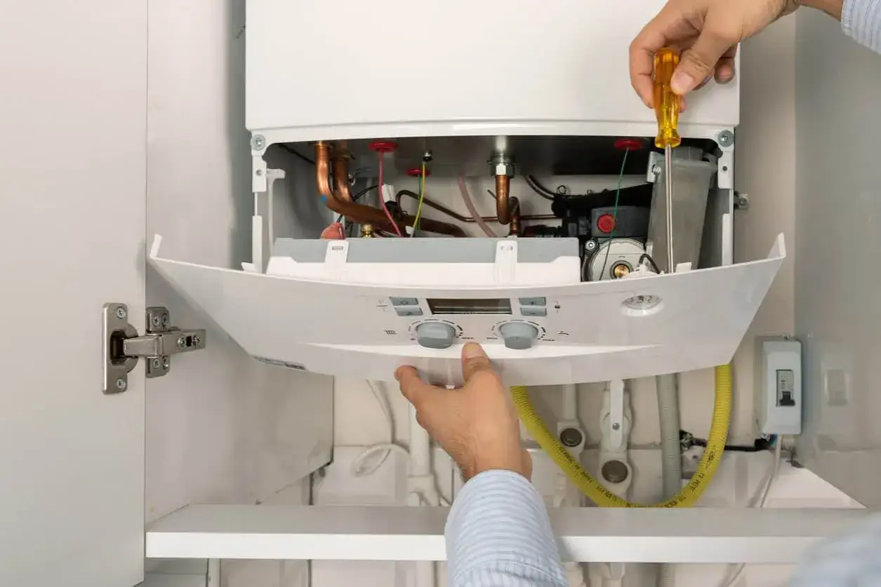 Installation d'une chaudière gaz pour ma prime renov. Un technicien ajuste l'appareil avec un tournevis.