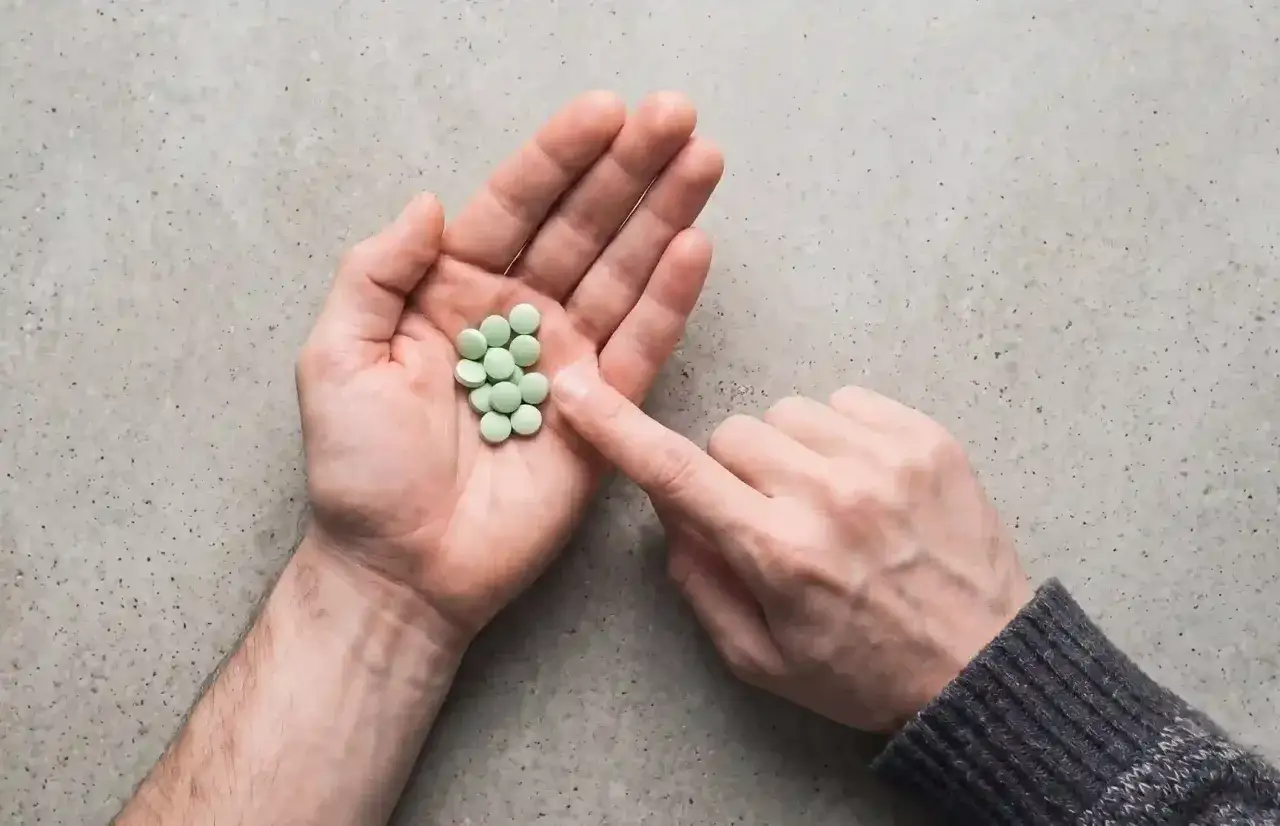 Mano aperta con un mucchietto di pillole verdi, come un trittico gocce. Un dito le sfiora.