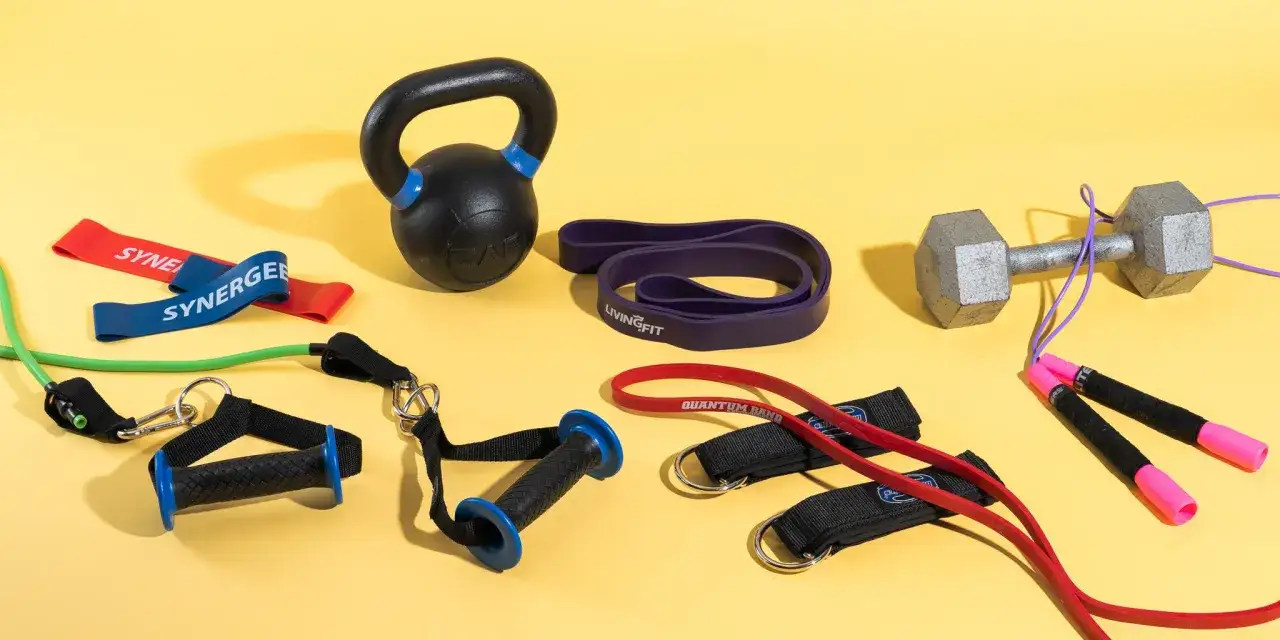 R&oacute;żne rodzaje gum do ćwiczeń, hantla, kettlebell i skakanka na ż&oacute;łtym tle.