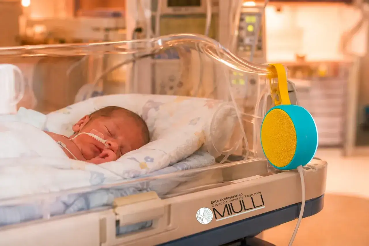 Un neonato dorme sereno nella terapia intensiva neonatale, con un piccolo altoparlante colorato che diffonde dolci melodie, sperando che il tempo in terapia intensiva neonatale sia il pi&ugrave; breve possibile.