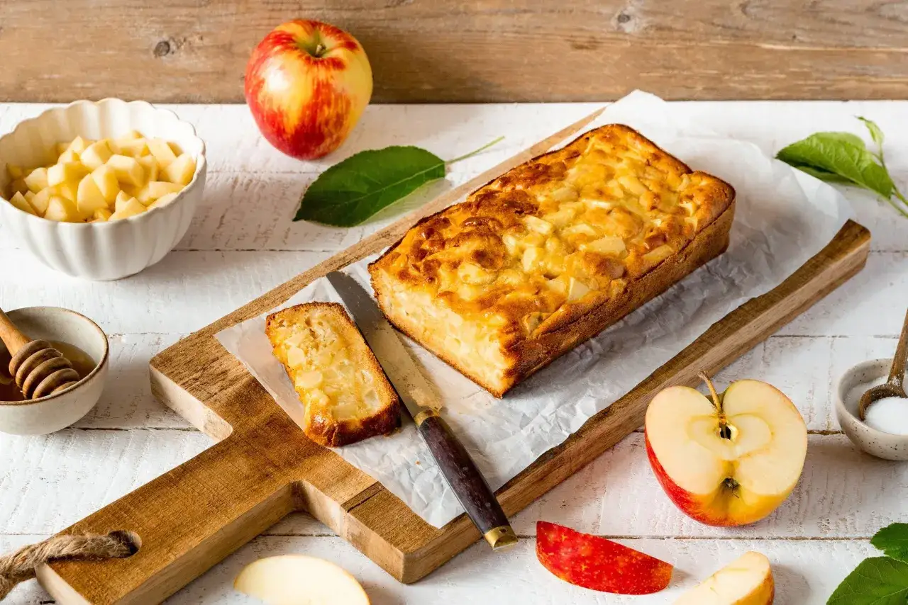 Un d&eacute;licieux g&acirc;teau aux pommes dor&eacute;, avec une tranche coup&eacute;e, des pommes fra&icirc;ches, du miel et du sucre.