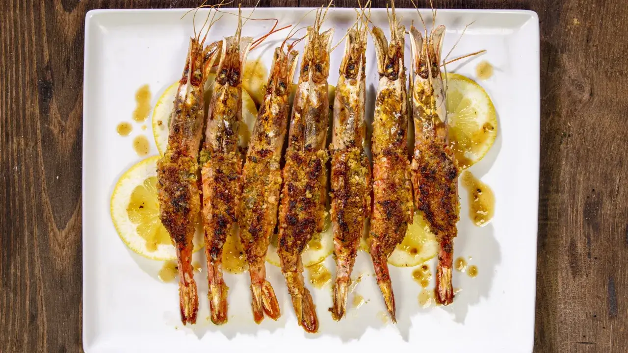 Sette gamberoni al forno dorati e croccanti, serviti su fette di limone e conditi con una salsa dorata.