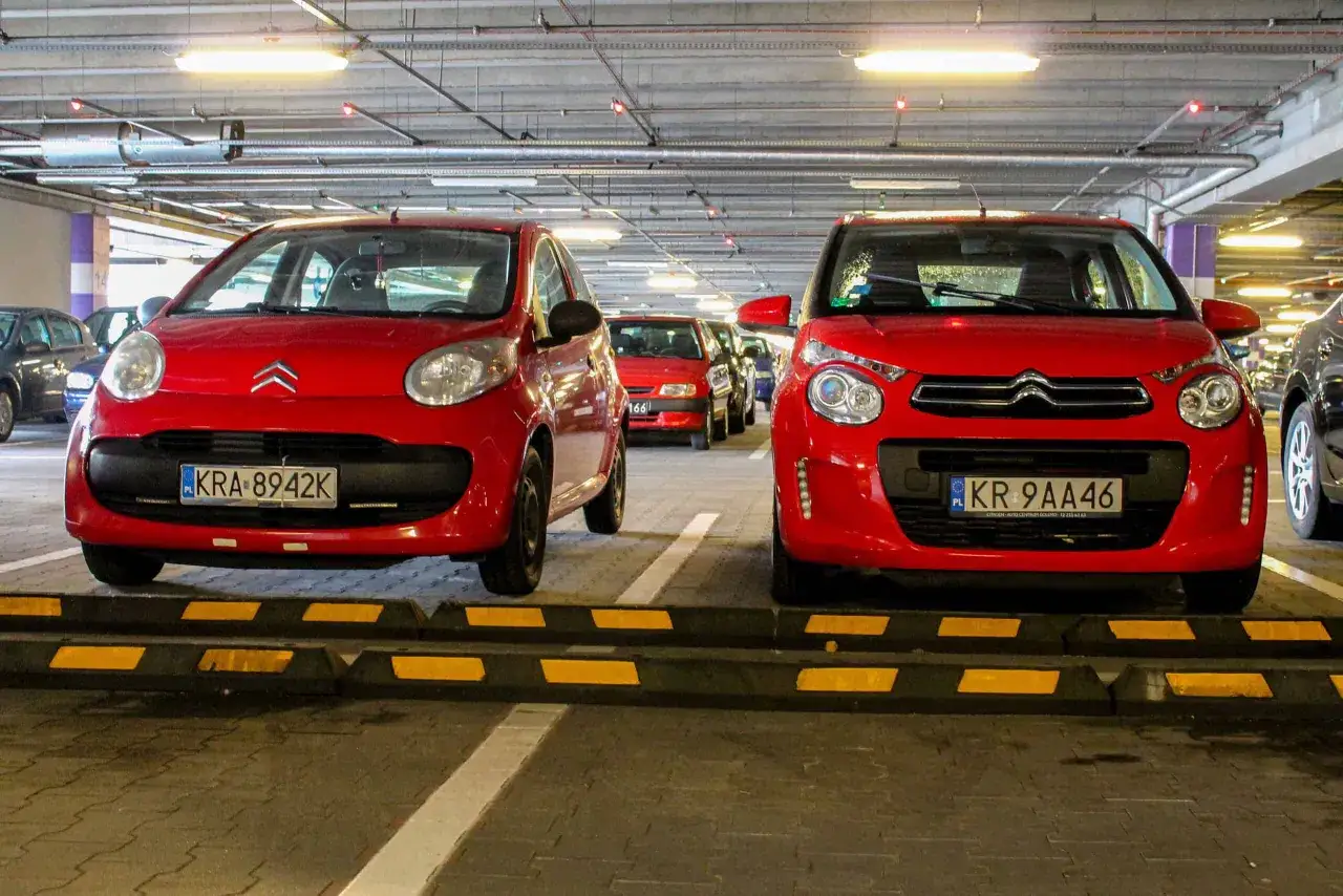 Dwa czerwone Citroen C1 stoją obok siebie na parkingu podziemnym.