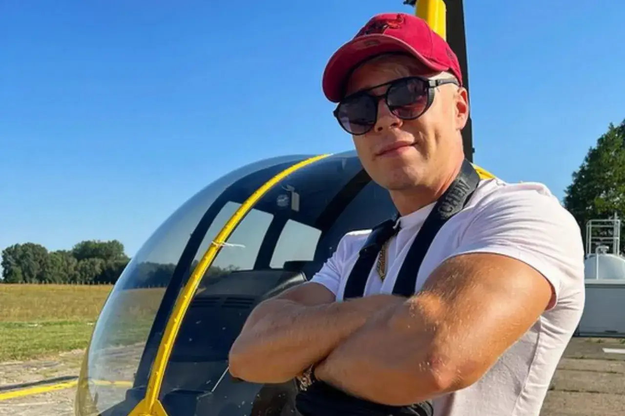 Mężczyzna w czerwonej czapce i okularach przeciwsłonecznych stoi przed helikopterem. Ciekawe, ile lat ma Skolim, że już lata helikopterem?