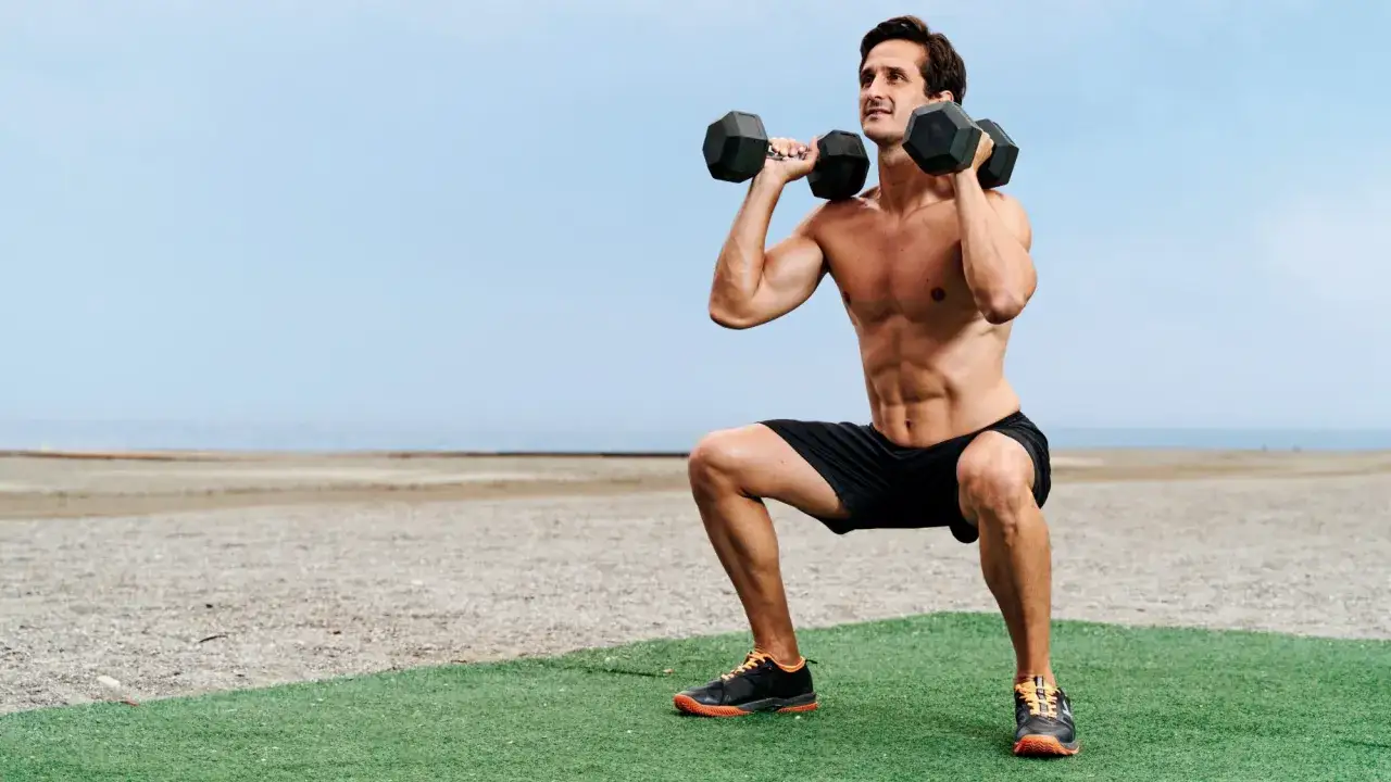 Mann macht ein Workout mit Hanteln am Strand.