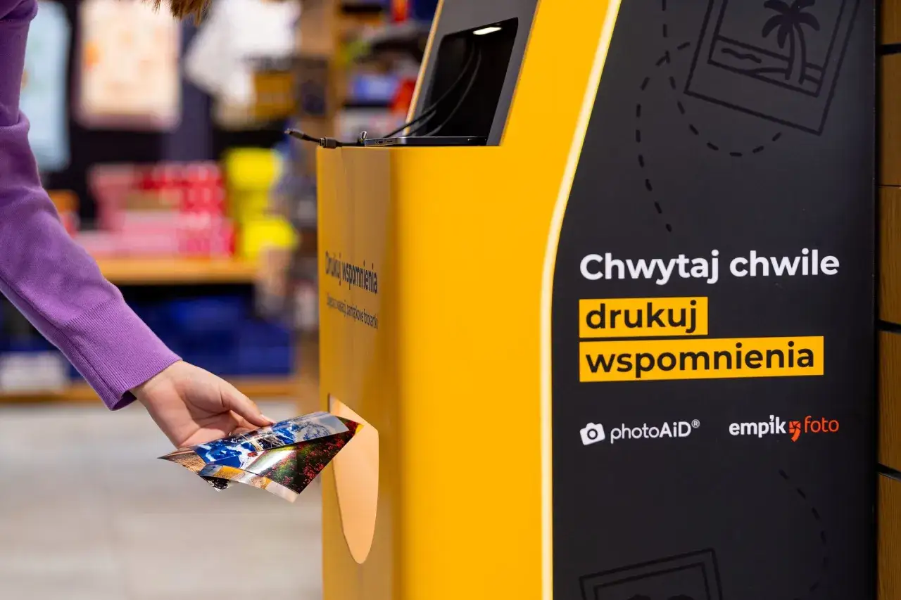 Ręka wkłada zdjęcia do automatu, by wydrukować wspomnienia w Empiku. Proste jak nigdy!