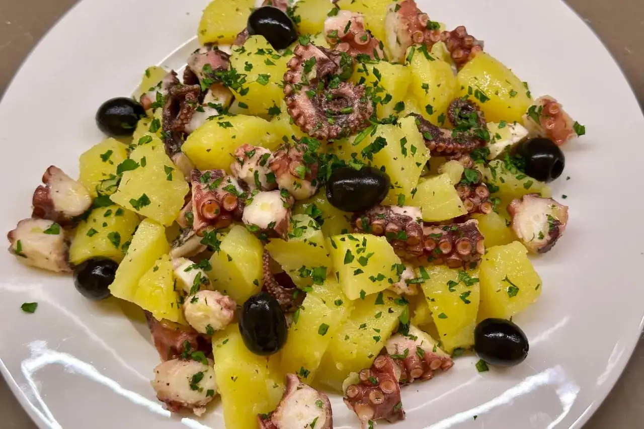 Deliziosa insalata polpo e patate, condita con prezzemolo fresco e olive nere, servita su un piatto bianco.