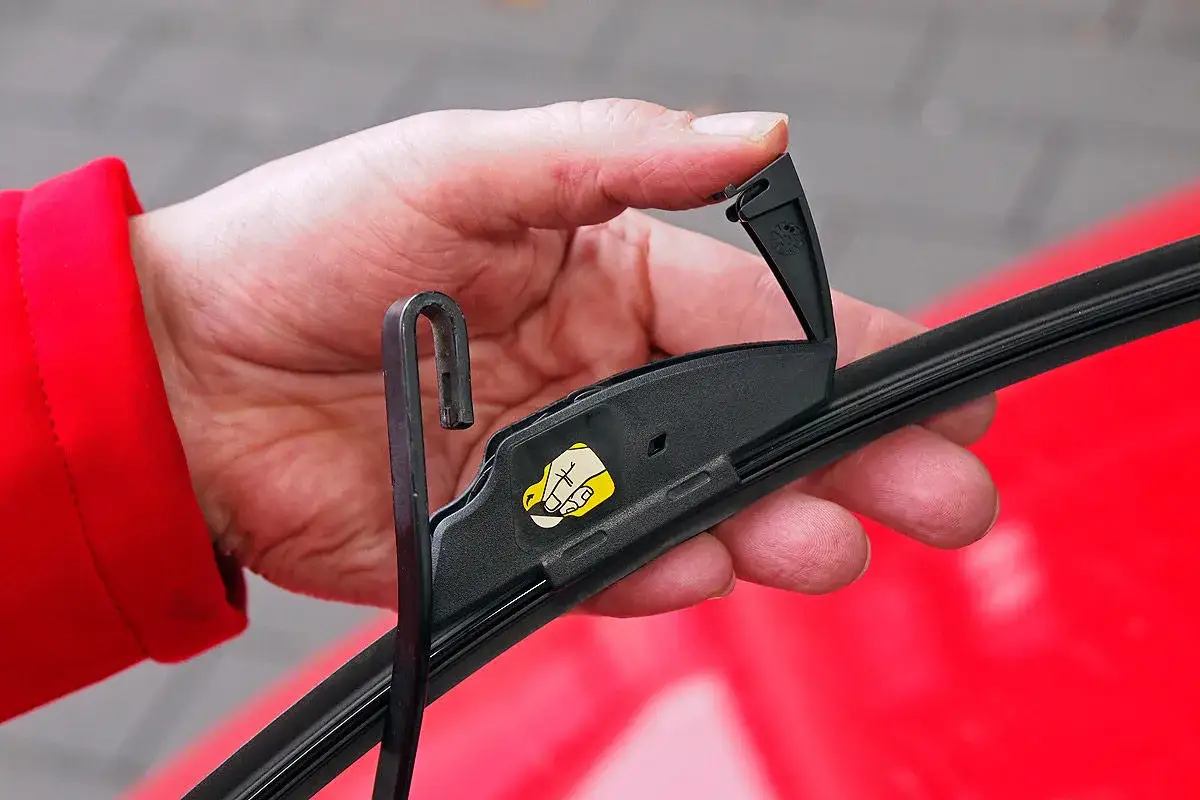 Hand wechselt Scheibenwischer an einem VW. Der Haken des Wischerarms wird in die Halterung eingef&uuml;hrt.