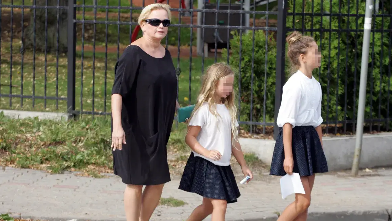 Katarzyna Figura z dwiema córkami idzie chodnikiem. Dziewczynki ubrane w białe bluzki i granatowe spódniczki.
