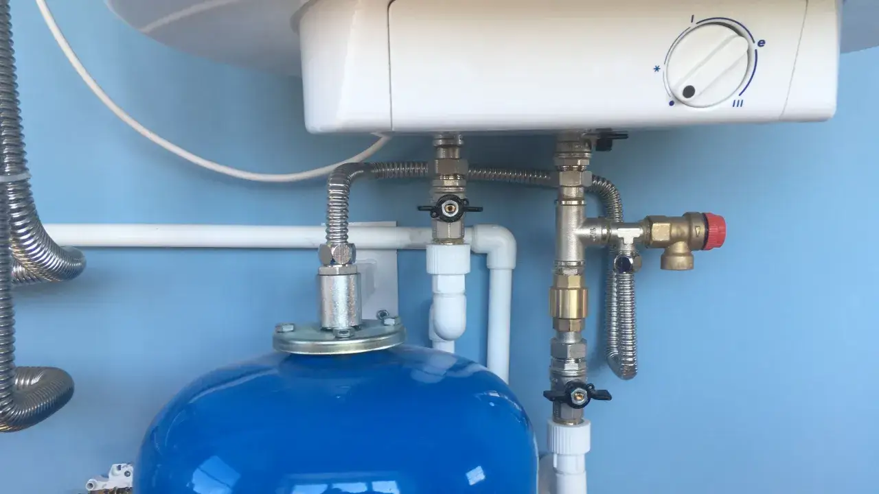 Schema montaggio vaso espansione scaldabagno: tubi, valvole e serbatoio blu collegati a un boiler bianco.