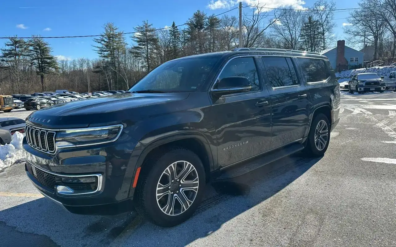 Ciemnoszary Jeep Grand Wagoneer zaparkowany na zewnątrz, z widocznymi innymi samochodami i drzewami w tle.