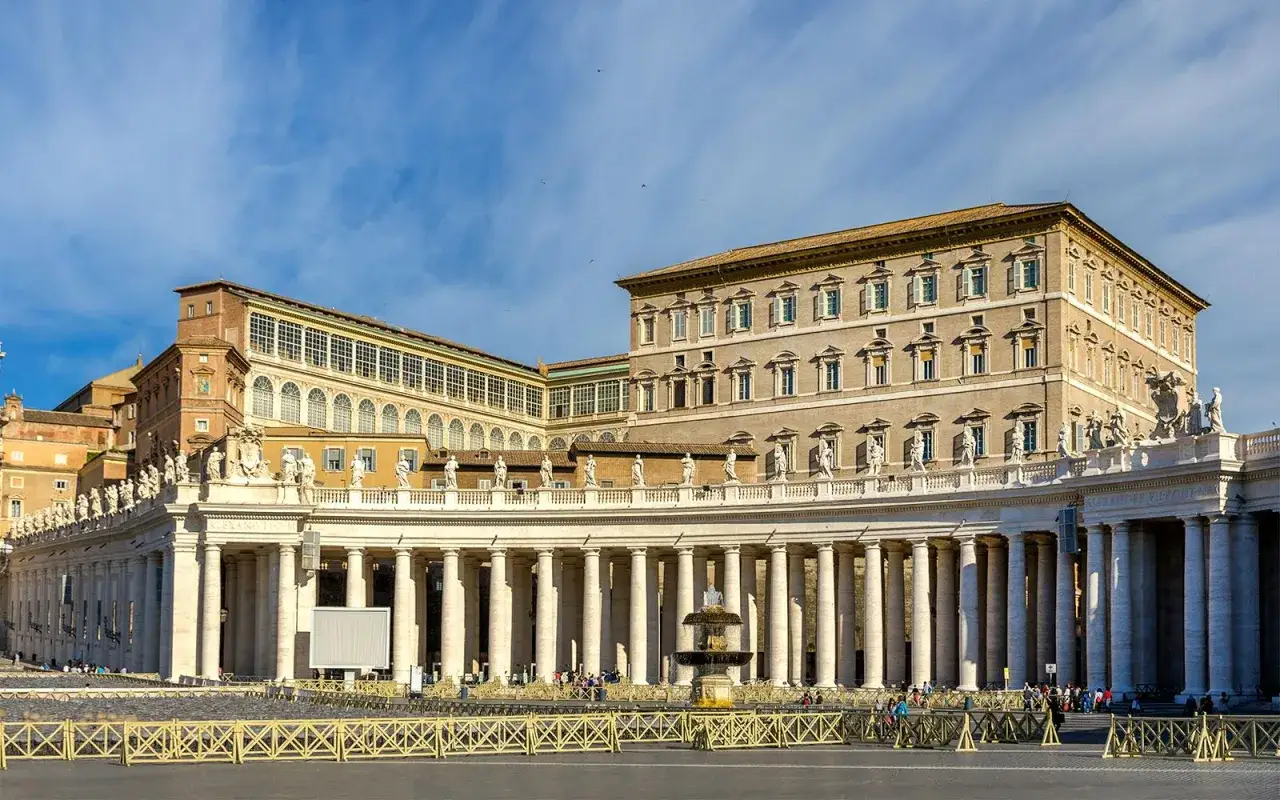 Der apostolische Palast, ein imposantes Geb&auml;ude mit S&auml;uleng&auml;ngen und Statuen, ragt unter blauem Himmel auf.
