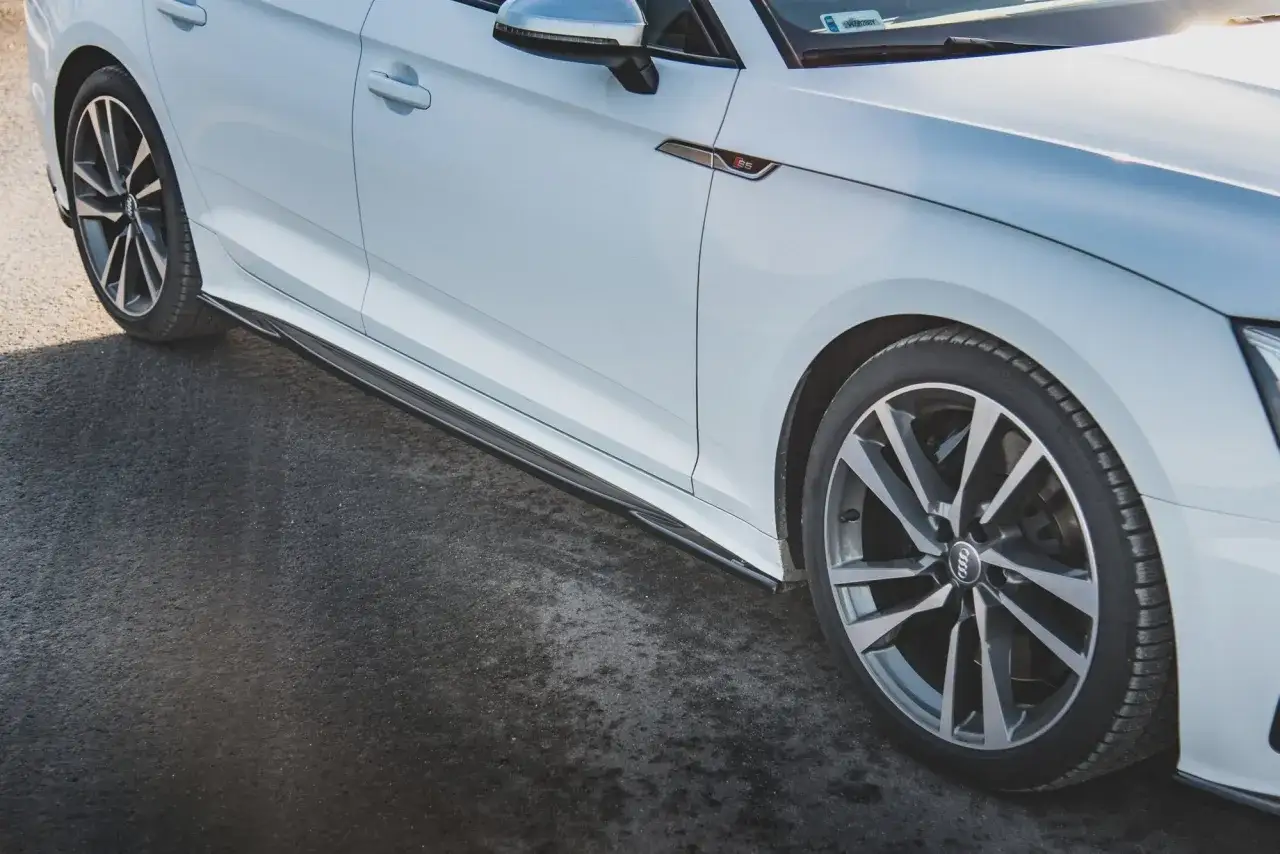 Białe Audi A5 F5 z czarnymi progami i felgami stoi na ciemnym asfalcie.