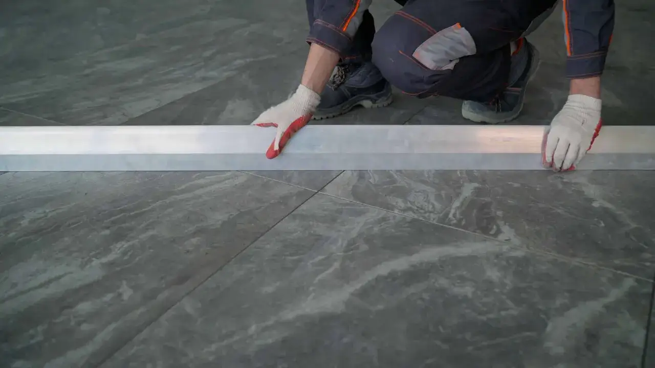 Man con guantes ajusta perfil met&aacute;lico sobre azulejos rectificados, evitando problemas de nivelaci&oacute;n.