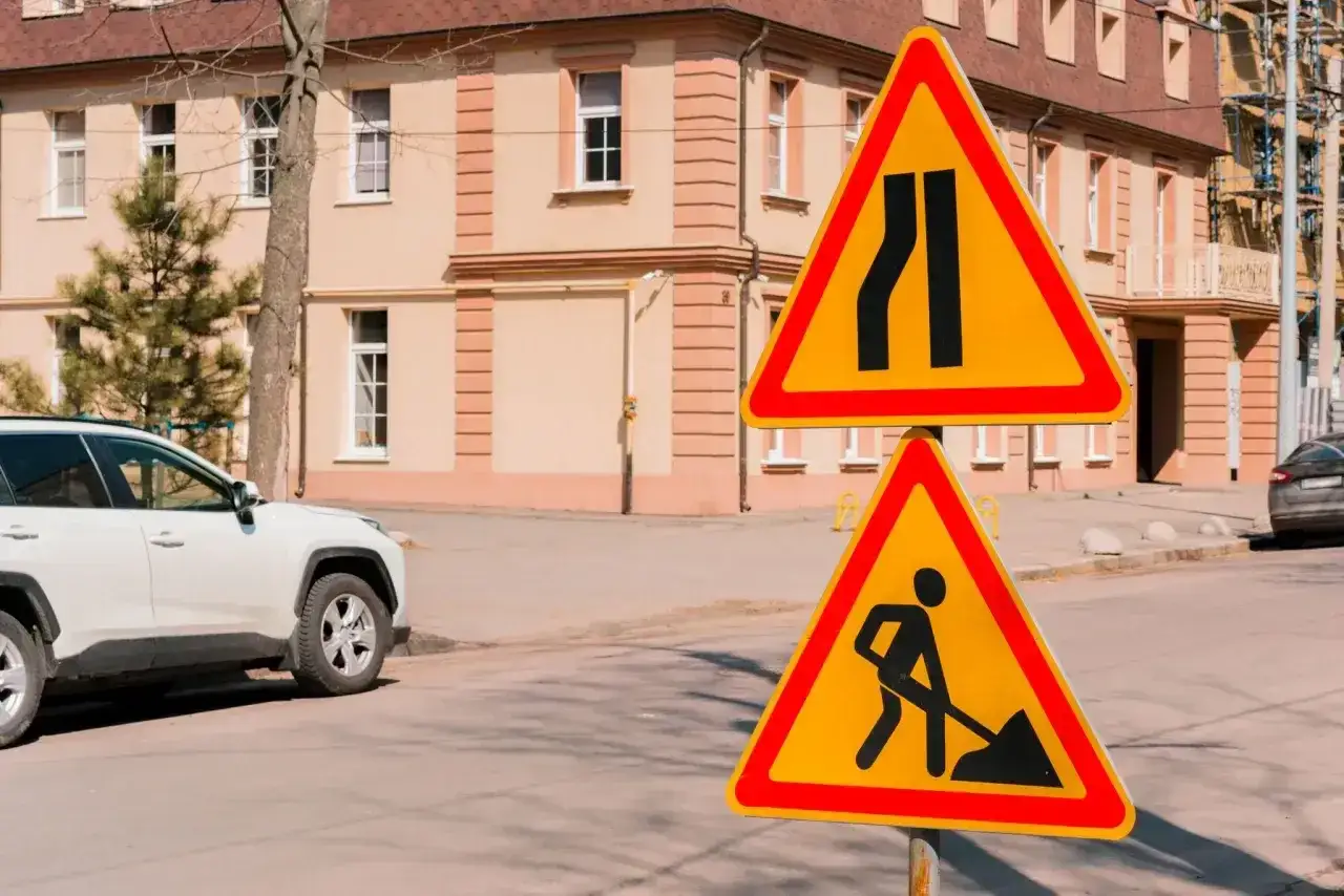 Znaki drogowe ostrzegają przed zwężeniem jezdni i robotami drogowymi. Czas na jazdę na suwak i ostrożność!