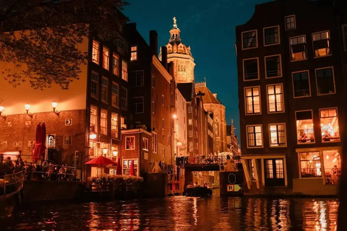 Un giro in barca serale lungo i canali di Amsterdam, con edifici illuminati e riflessi sull'acqua. Magia di Amsterdam by night.