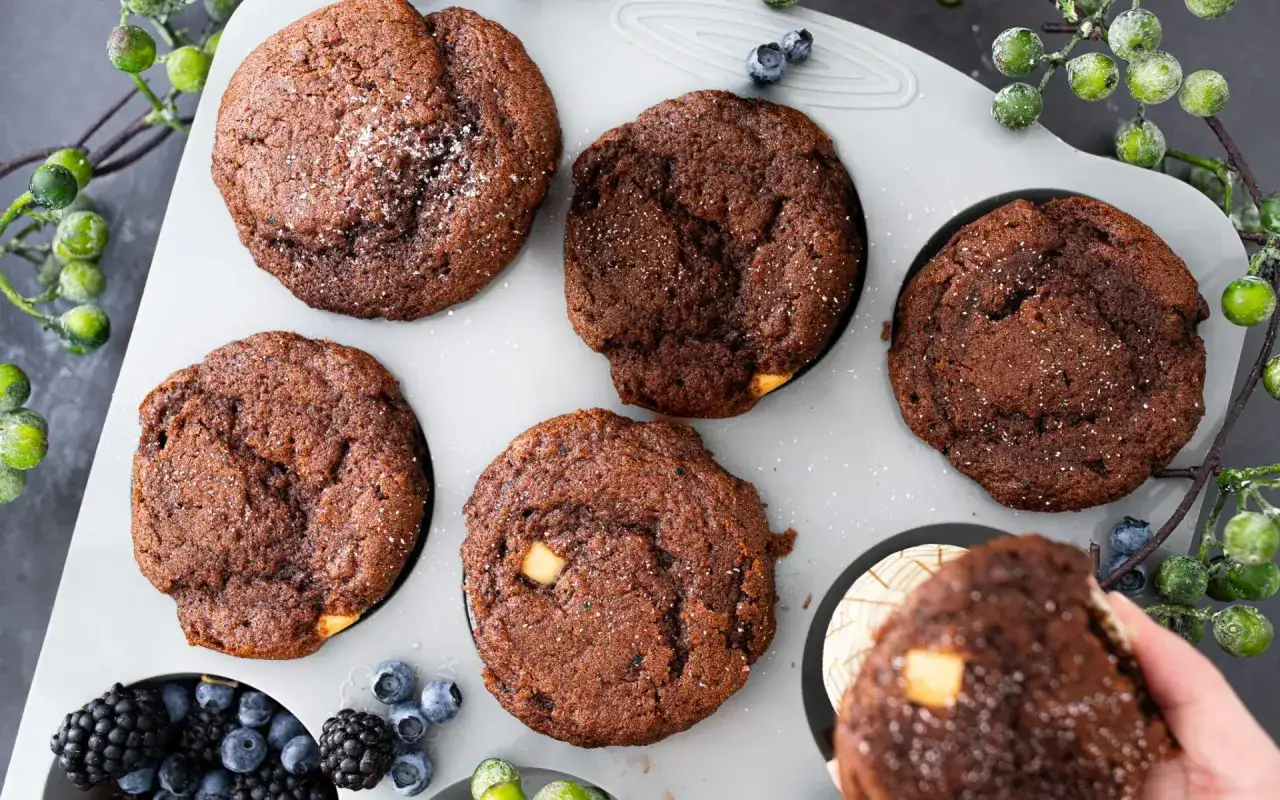 Schokomuffins rezept: Saftige Schokomuffins mit weißen Schokostückchen in einer Muffinform, garniert mit Beeren und grünen Beeren.