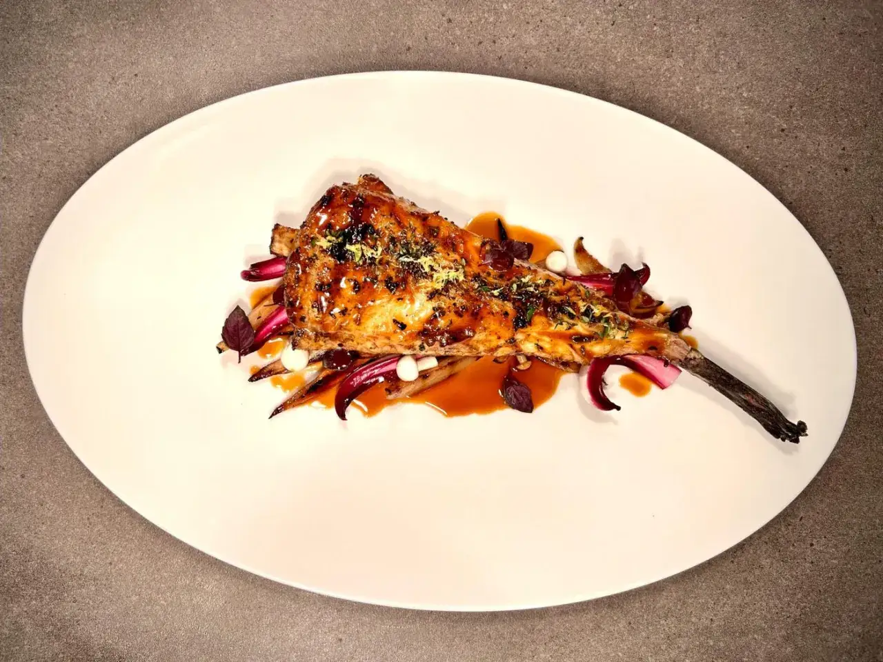 Lotte au barbecue, nappée d'une sauce caramélisée, servie sur des légumes croquants et des éclats de citron. Un délice visuel et gustatif.
