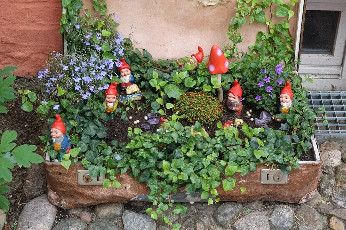Ein alten Koffer bepflanzen mit Gartenzwergen und Blumen. Efeu rankt sich um den Koffer, der als Blumenbeet dient.
