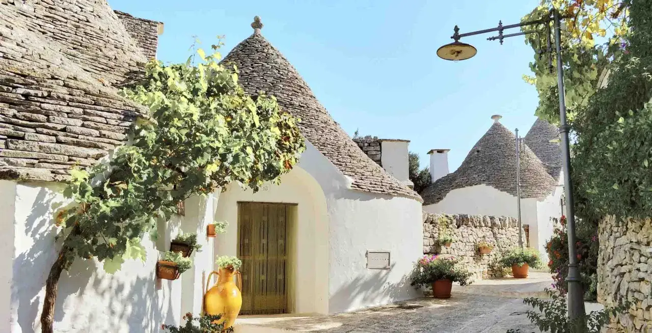 Trulli bianchi e tetti conici in pietra nel Val d'Itria, con un vaso giallo e piante rampicanti.