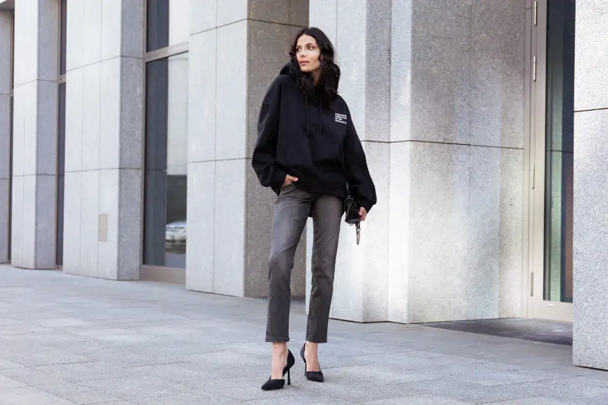Donna con felpa nera oversize e jeans grigi, un look che esprime il **loose fit significato** di comfort e stile moderno.