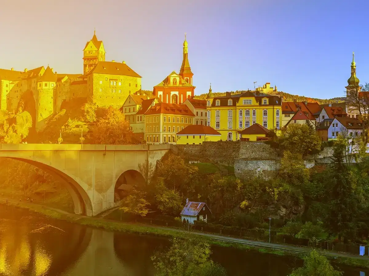 Złote światło zalewa malownicze stare miasto Czech z zamkiem, mostem i rzeką.