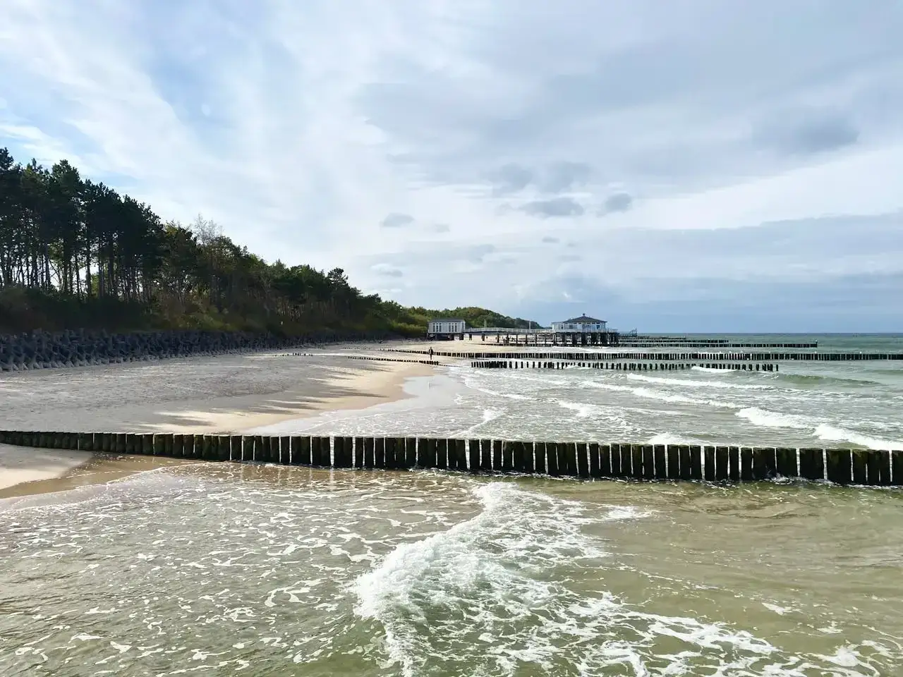 Majówka nad morzem zapowiada się pochmurnie, ale plaża z drewnianymi falochronami i lasem w tle jest urokliwa.