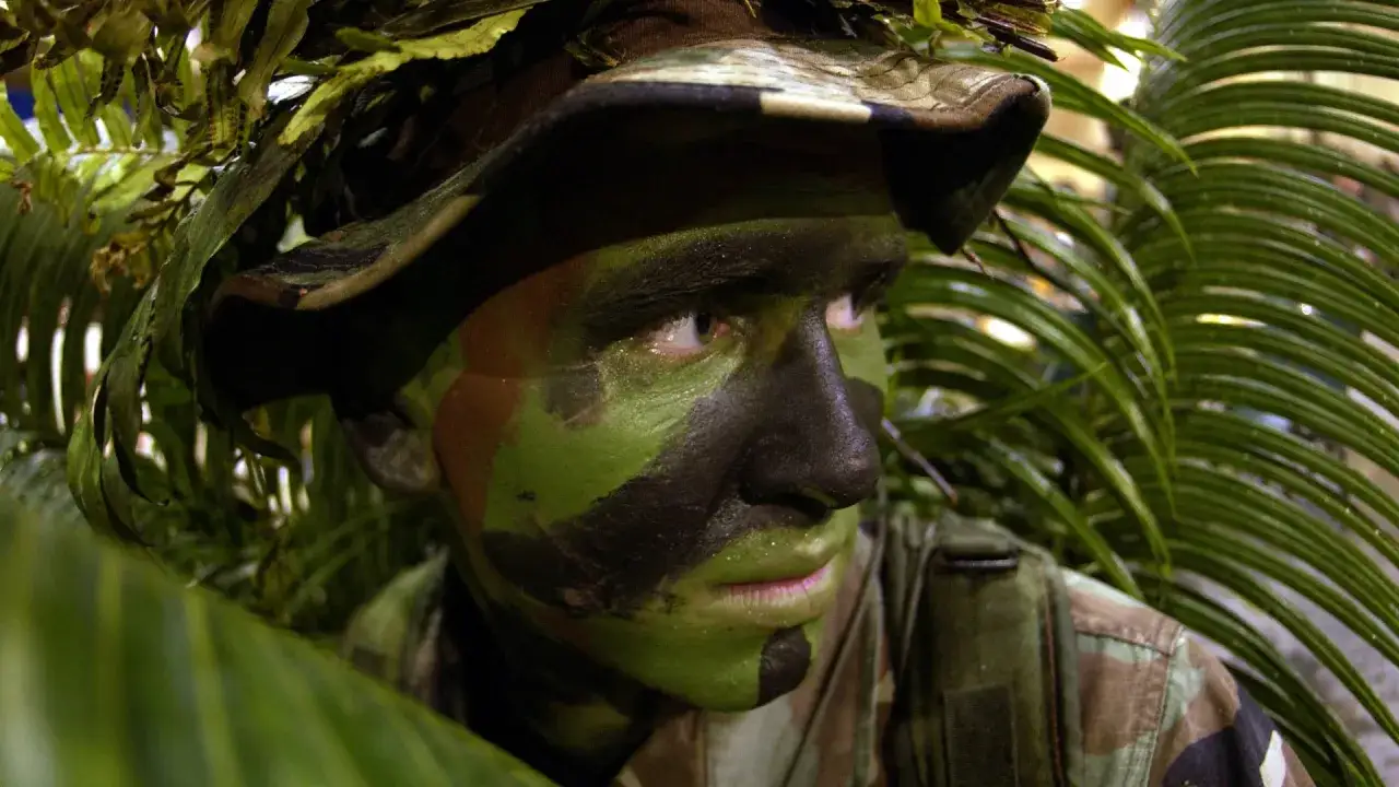 Soldado con rayas militares en la cara, camuflado entre la vegetaci&oacute;n, listo para la misi&oacute;n.