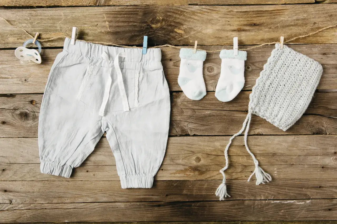 Niebieskie ubranka dziecięce, w tym spodenki, skarpetki i czapeczka, wiszą na sznurku. Czy ubranka dziecięce od znanej mamy-celebrytki są miłe w dotyku?