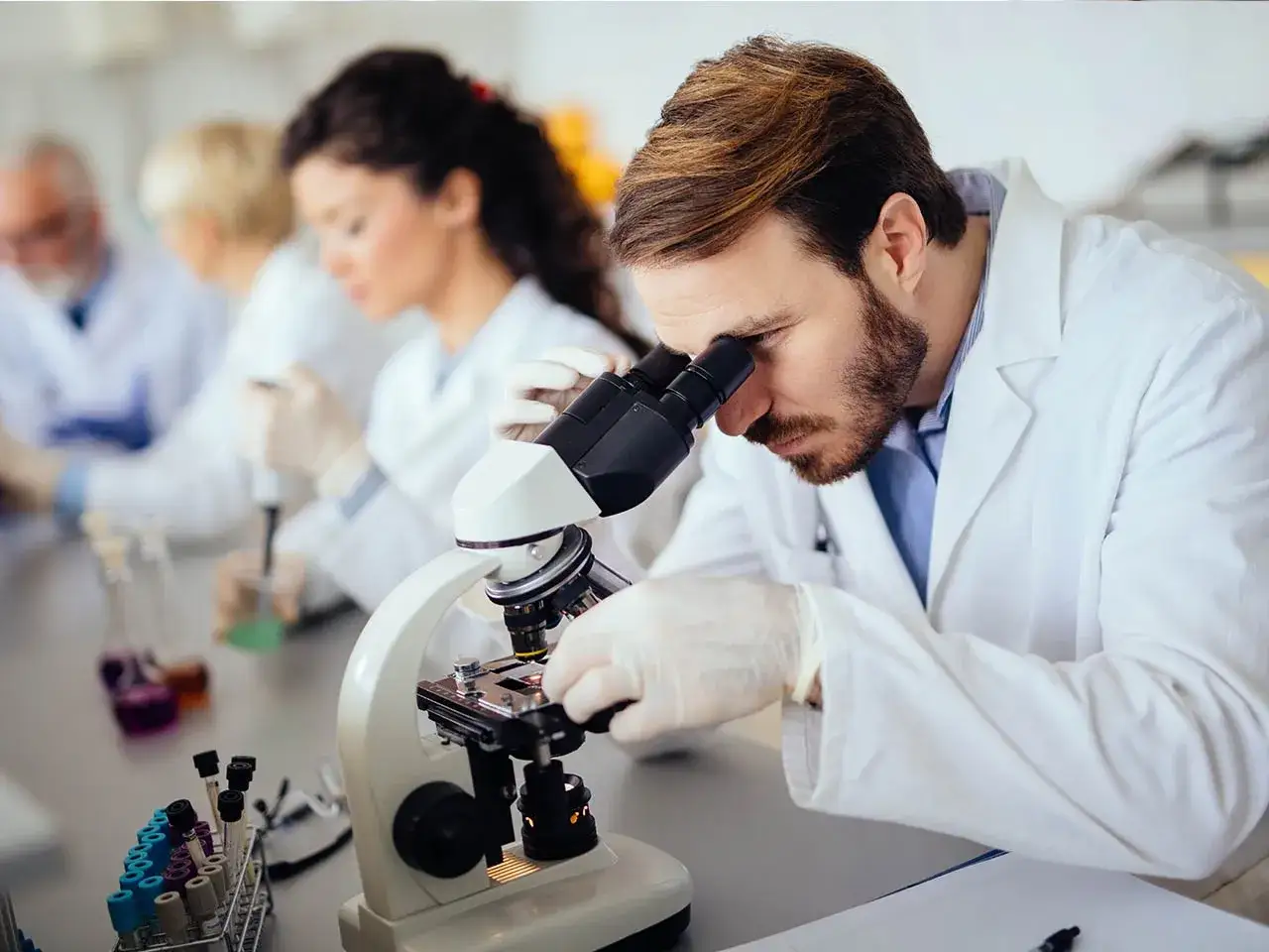 Ricerca scientifica in laboratorio: un biologo nutrizionista osserva al microscopio, con colleghi impegnati in esperimenti.
