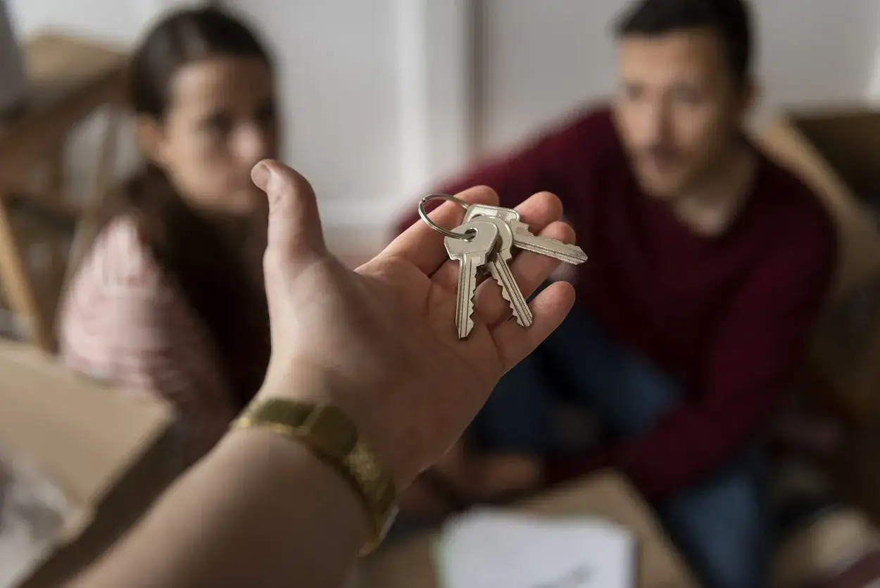Mano entrega llaves. Pareja sonríe, lista para recuperar vivienda alquilada para un hijo. Mudanza.