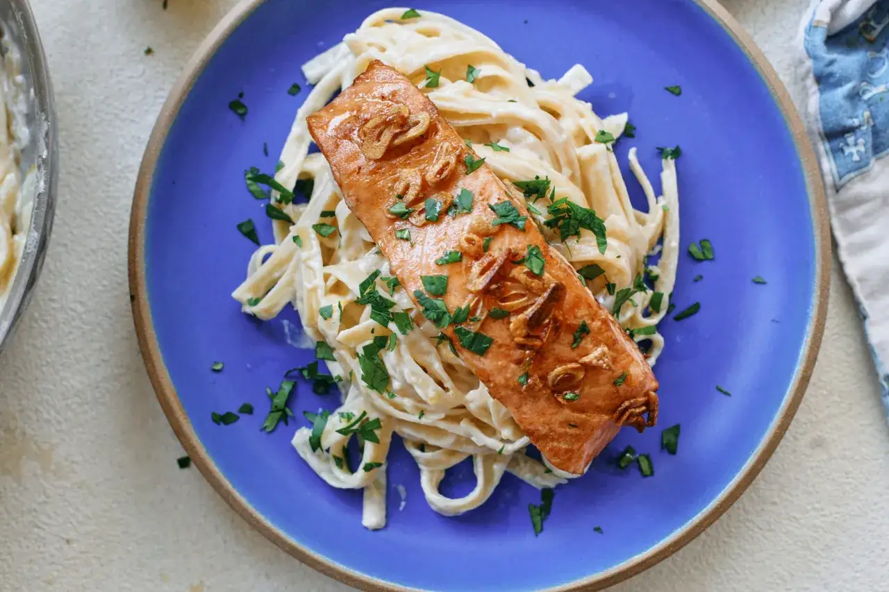 Ein saftiges Lachsfilet auf cremiger Pasta mit Lachs Sahne Sauce, garniert mit Petersilie und Knoblauch.